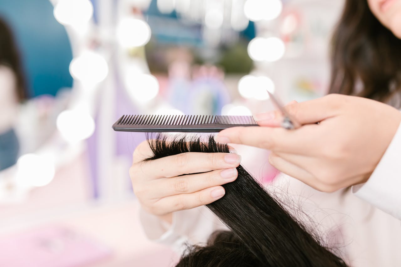 Close-up of a hairdresser grooming hair with scissors and a comb in a salon setting.